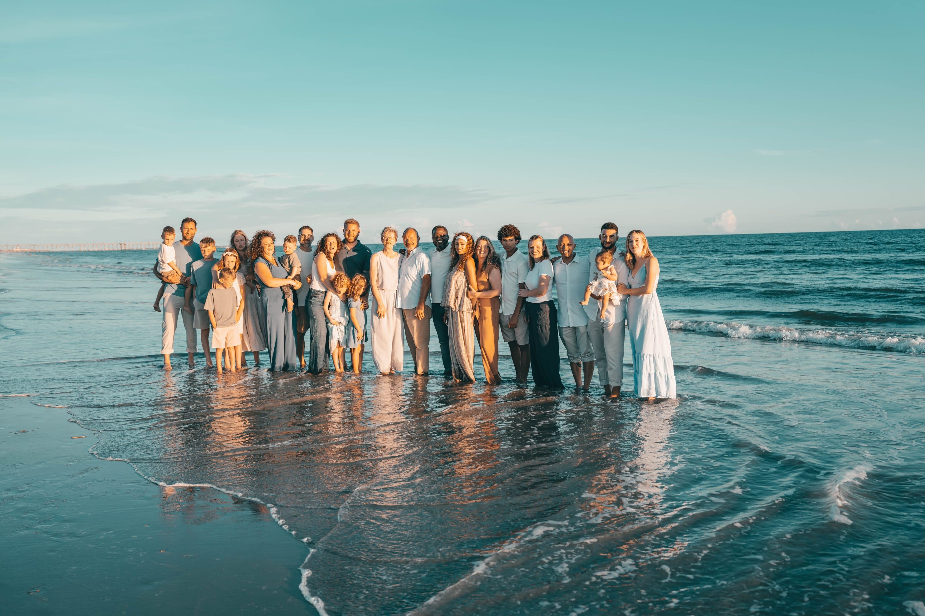 A multi-generational family standing together in the ocean surf